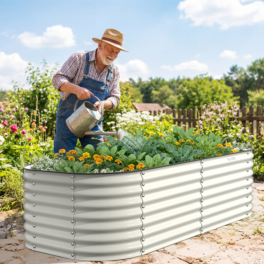 Man watering plants in a large metal garden bed in a garden setting.