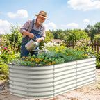 Man watering plants in a large metal garden bed in a garden setting.